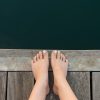 woman's feet on wooden pier overlooking water
