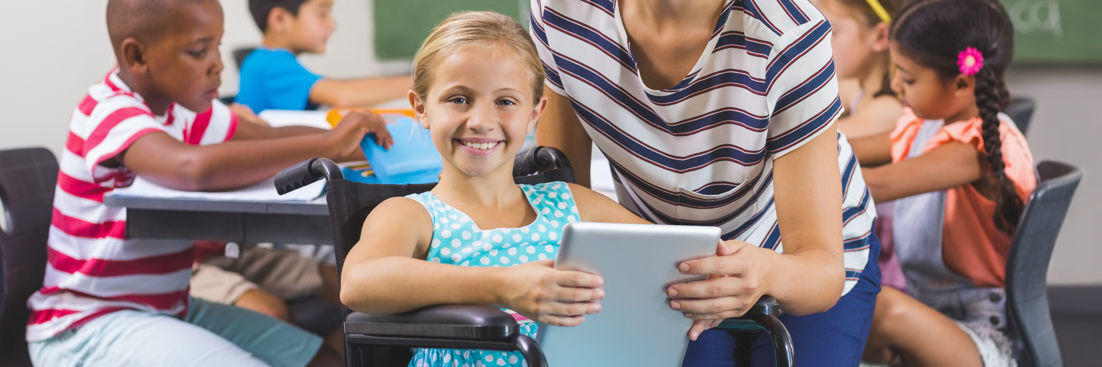 Girl and teacher using AAC tablet in classroom.