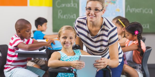 Girl and teacher using AAC tablet in classroom.