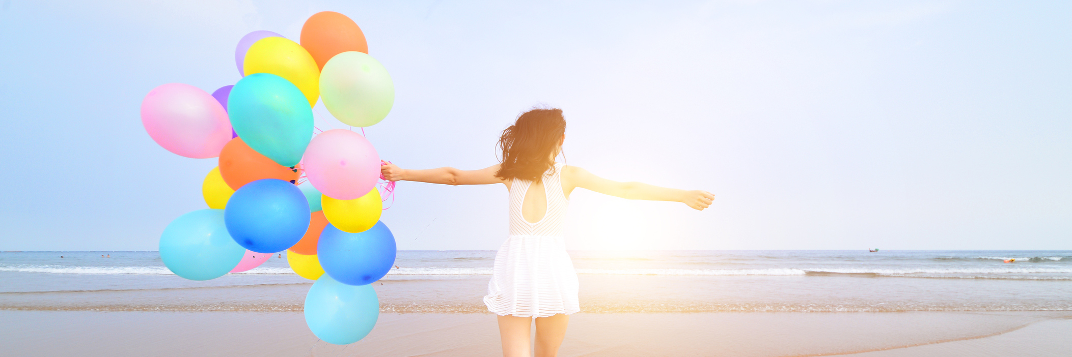 I Thought My Chronic Illness Was My Greatest Weakness, But I Was Wrong Woman at the beach, walking on the shore with vibrant balloons.