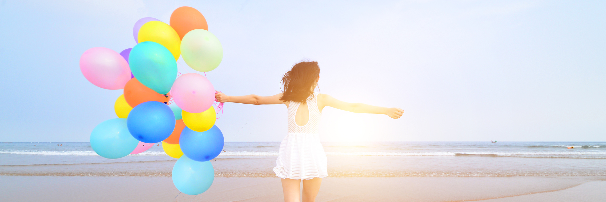 Woman at the beach, walking on the shore with vibrant balloons.