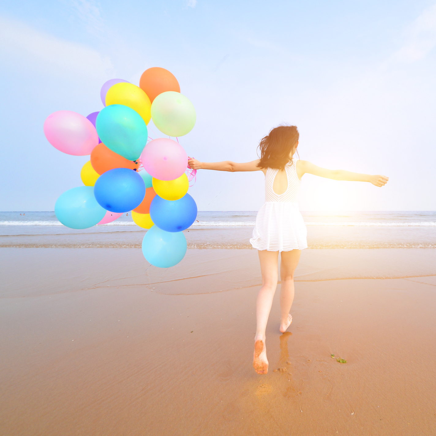 Woman at the beach, walking on the shore with vibrant balloons.