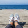 Woman feet in casual shoes on the wooden pier with sea or ocean background