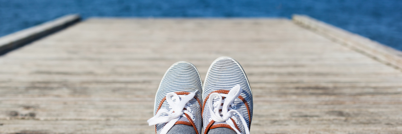 Anxiety and Depression Taught Me to Live in the Present Woman feet in casual shoes on the wooden pier with sea or ocean background