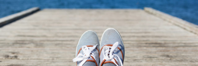 Woman feet in casual shoes on the wooden pier with sea or ocean background