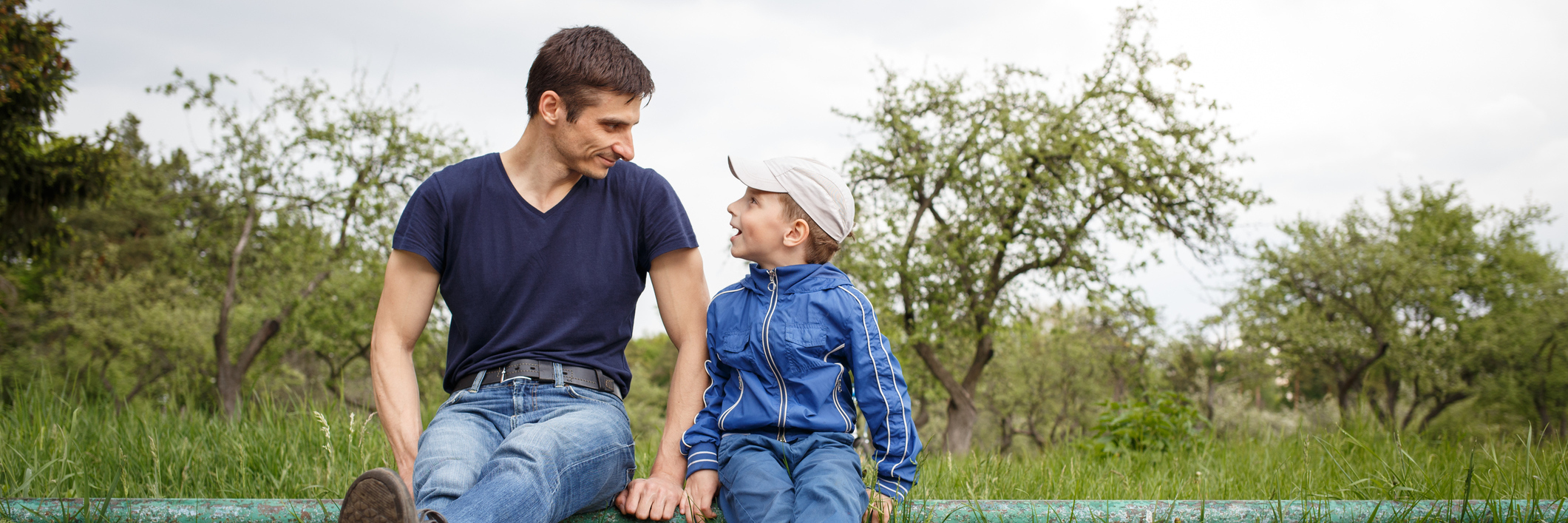 How to Talk to Children About Self-Harm Happy father and son sitting in the park. Smiling young man spending time together with his son