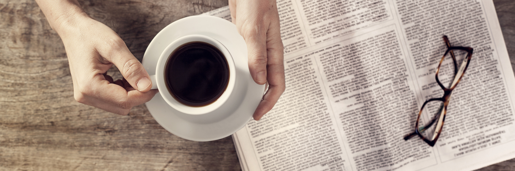 Young woman reading newspaper and holding coffee cup