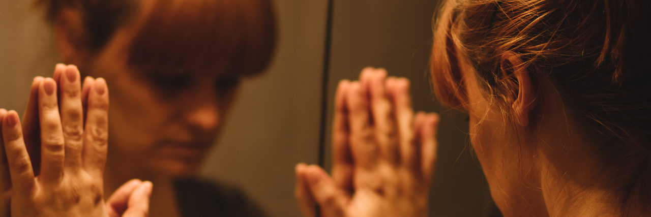 The Truth Behind Body Dysmorphia Sad and lonely woman looking at her reflection in the mirror