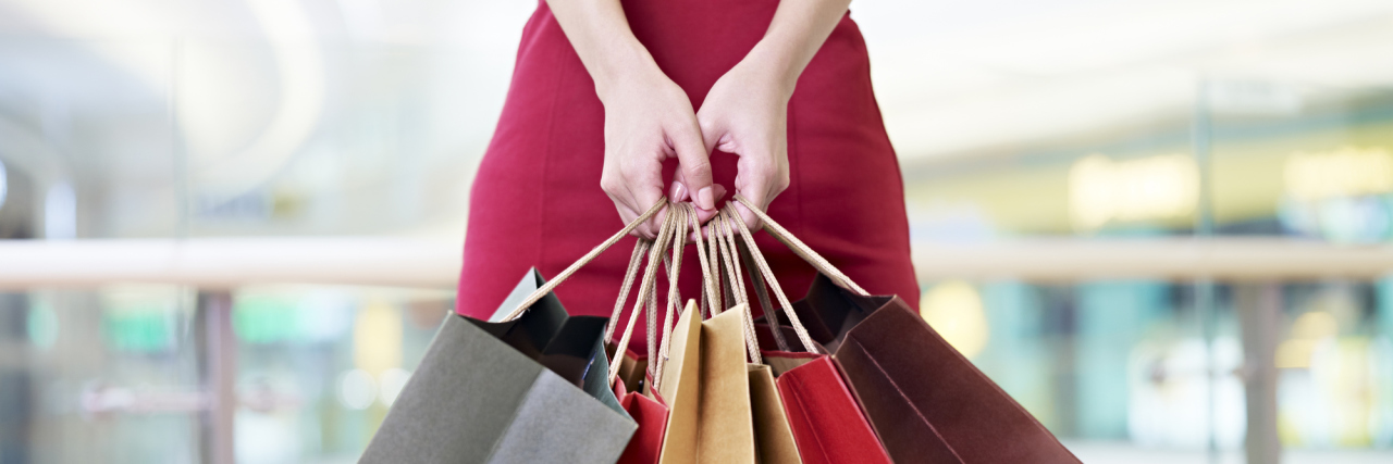 young woman female shopper standing with colorful paper bags in hands in shopping mall or department store, focus on hands