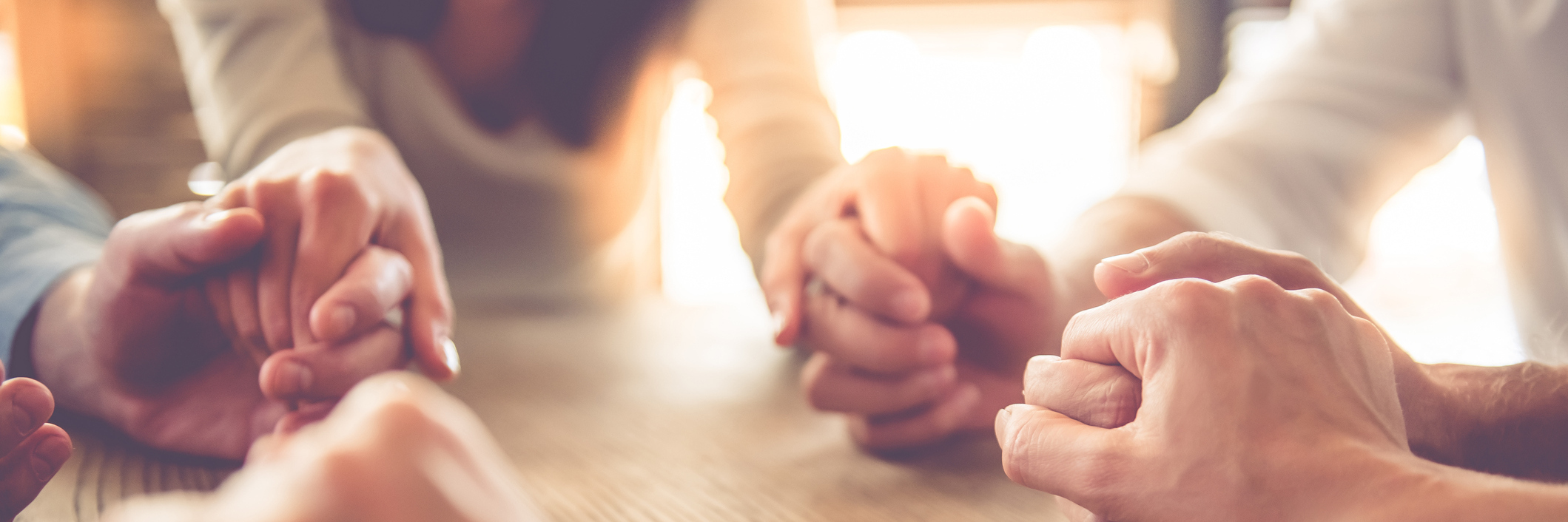 How I Found Mental Health Support in an Unlikely Place close up image of business team holding hands together on wooden table in warm light