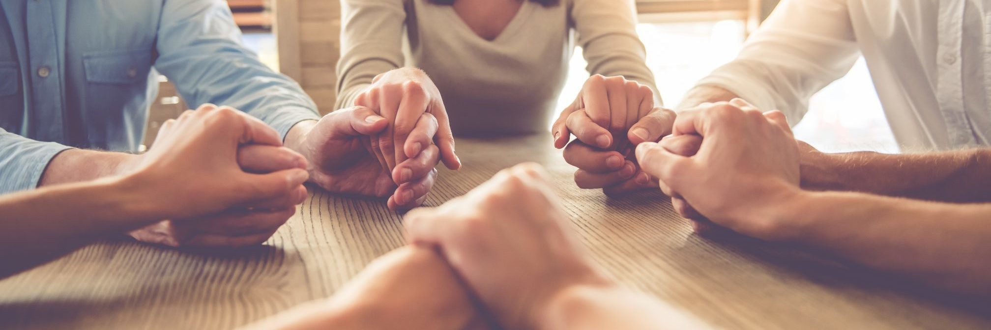 group of people holding hands around table in soft light