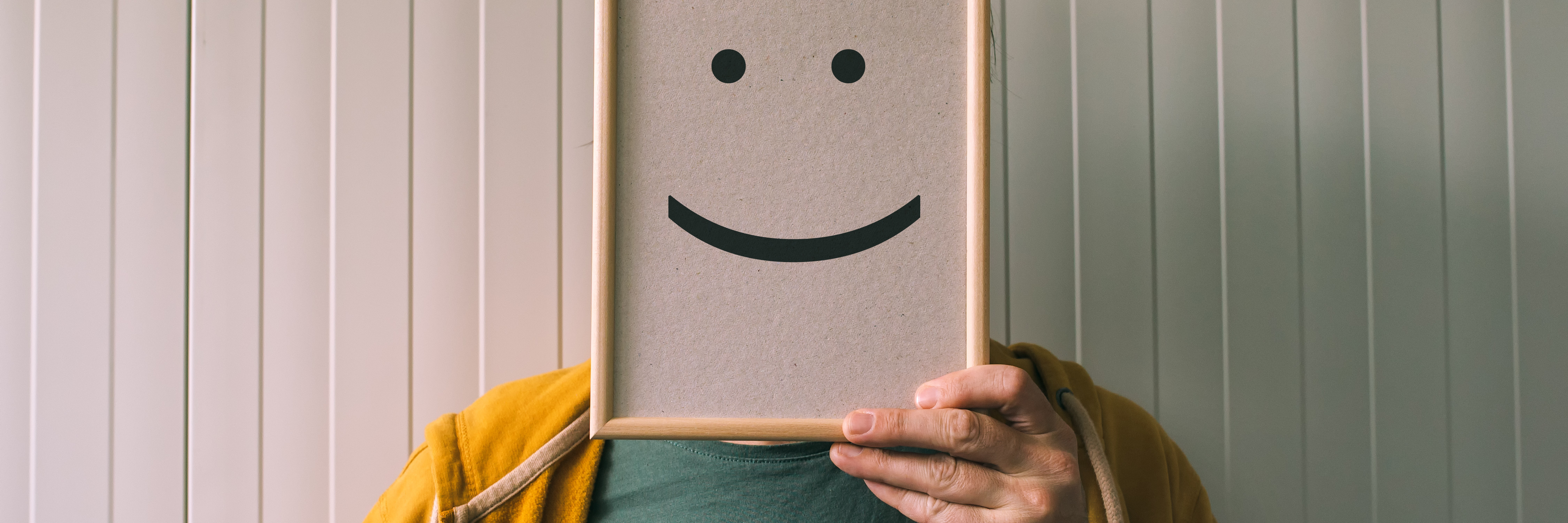 Hiding Behind Humour With Depression, Anxiety and PTSD man hiding face with whiteboard with smile drawn on