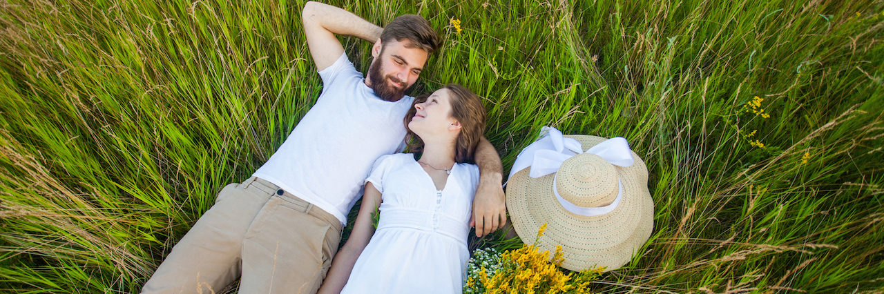 Happy young relaxed couple in love laying down on the grass overhead
