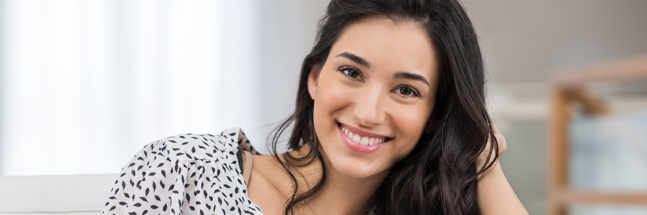 Why to Be Kind to Your Body If You Have a Chronic Disease Woman sits on the couch, look at the camera with a smile on her face.