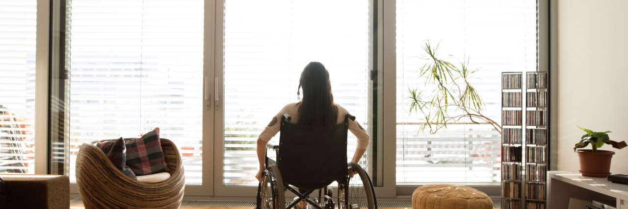 Study Says Airbnb Hosts More Likely to Reject Guests With a Disability Young disabled woman in wheelchair at the window at home in a living room.