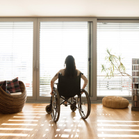 Young disabled woman in wheelchair at the window at home in a living room.