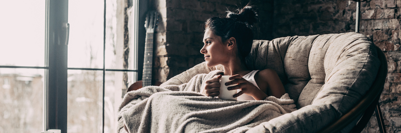 Anxiety Makes Me Cancel Plans Because I Can’t Handle ‘Uncomfortable' A woman sitting on a chair covered with a blanket