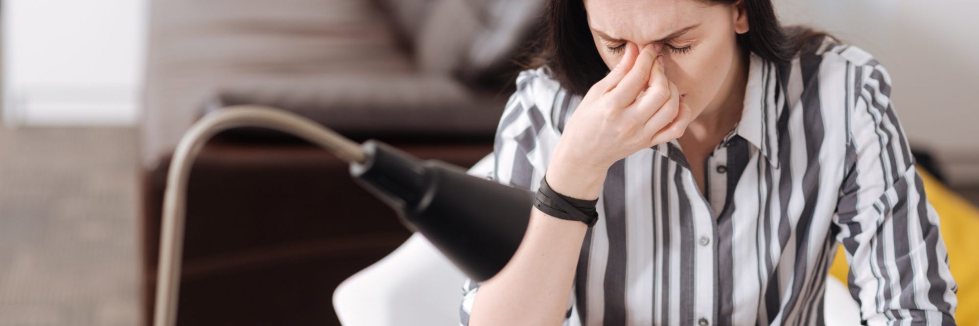 What to Do When Anxiety Strikes female office worker with fingers pressed to bridge of nose, striped shirt, looking stressed or anxious