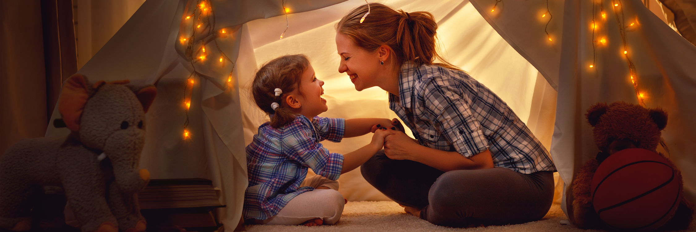 A mother and daughter under an indoor tent with lights.