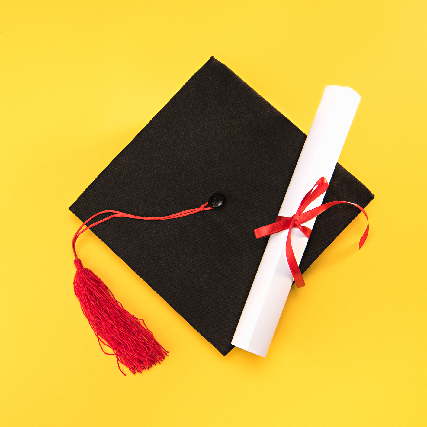 Top view of graduation mortarboard and diploma on yellow background.