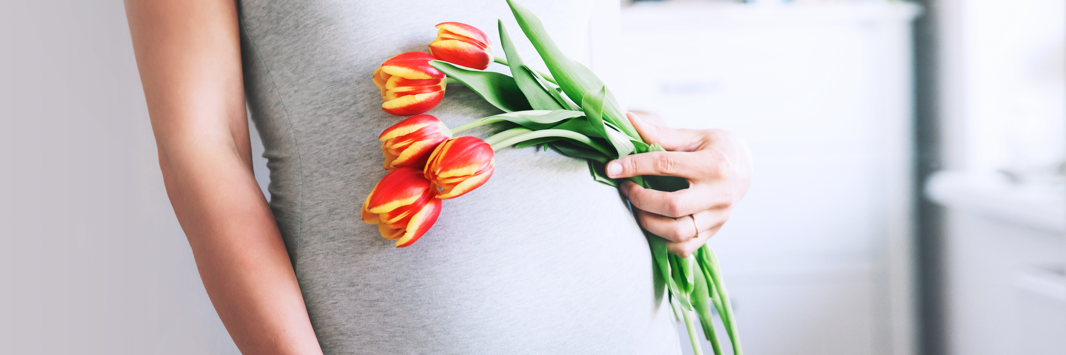 pregnant woman holding orange tulips with hands on belly