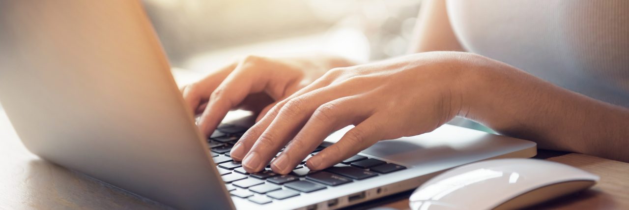 A Letter To My Internet Friend Struggling With Depression Closeup woman's hands typing on a laptop that is on a wooden desk with a mobile smartphone and mouse computer