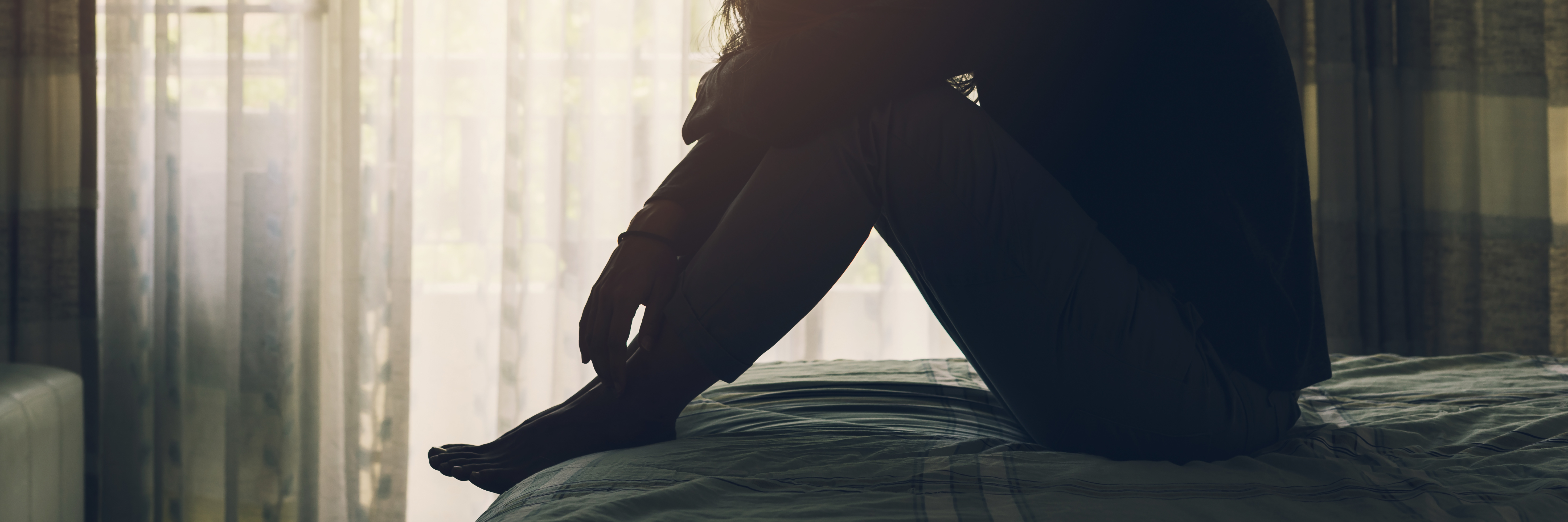 woman with depression sitting on bed in dark bedroom