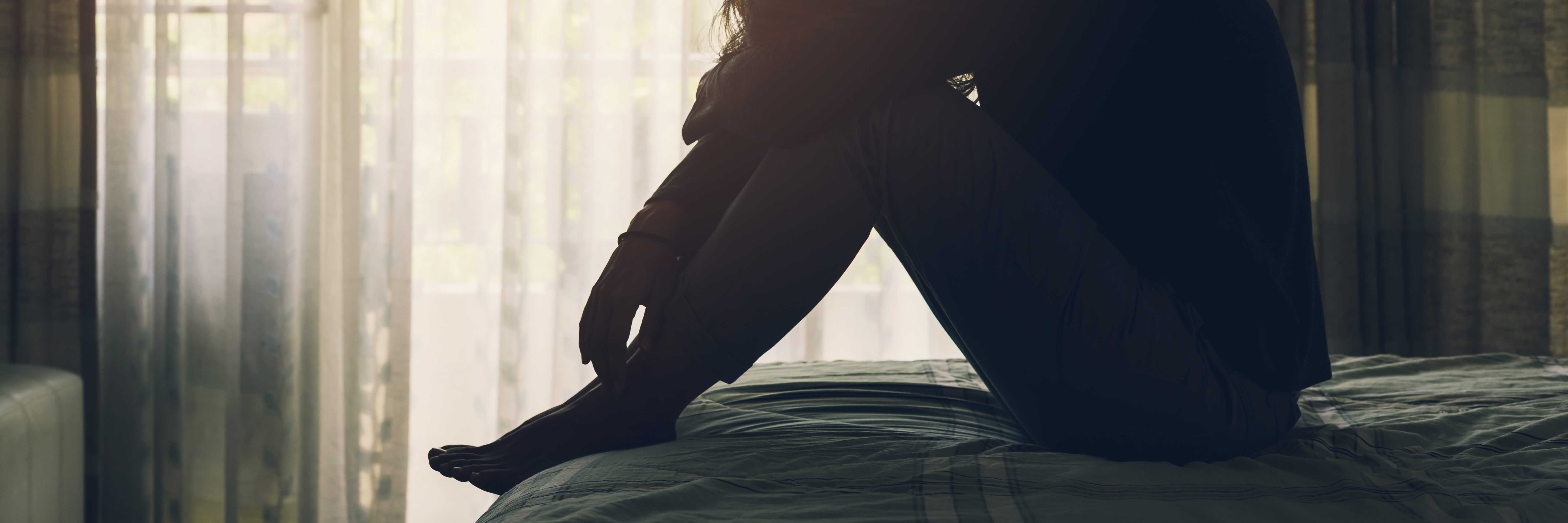 When Depression Makes You Feel Guilty for 'Wasting Time' woman with depression sitting on bed in dark bedroom