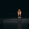 female actor alone on stage barefoot sitting on chair