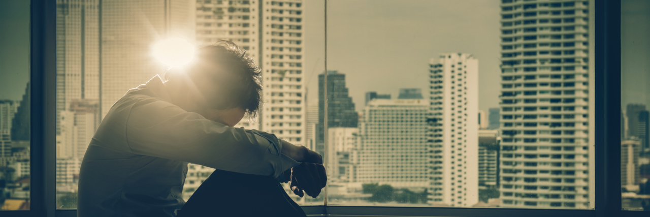 Defining Schizophrenia: Biological, Spiritual, and Environment Factors upset man in front of window with skyscrapers and lens flare