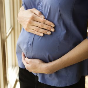 Pregnant woman wearing a denim shirt holding her belly