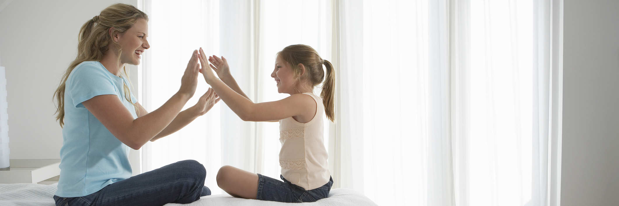 mother and daughter sitting on a bed and playing games