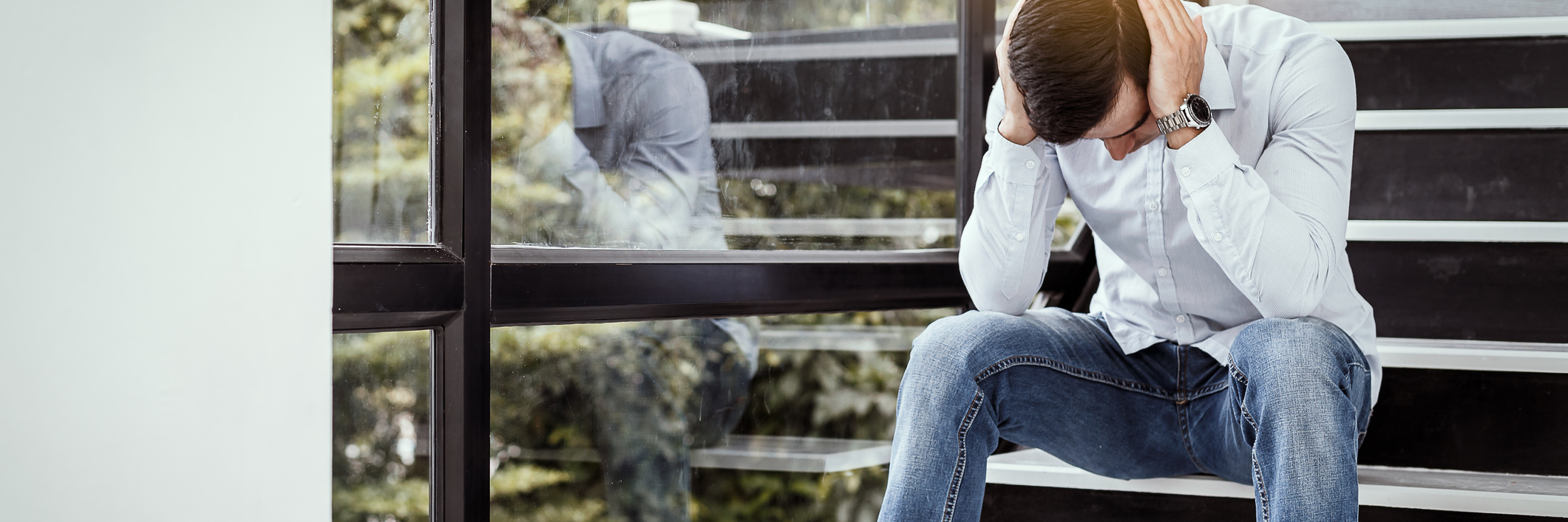 How Breathing Helps Panic Attacks young man sitting on staircase near window holding head in despair or anxiety