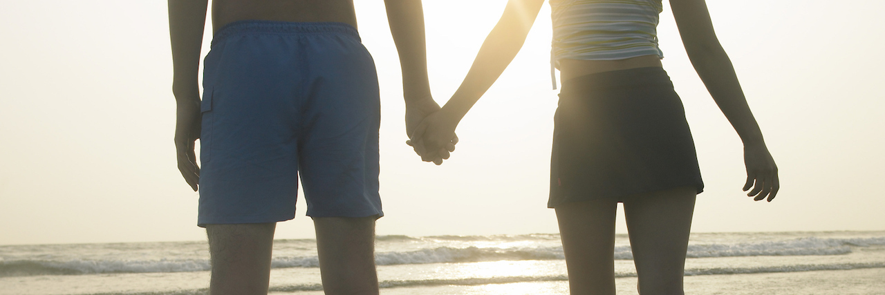 How I Manage a Healthy Relationship With PTSD A couple holding hands at the beach