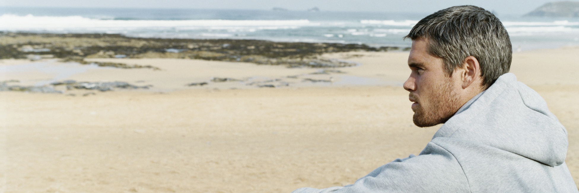 Pityriasis Lichenoides (PLEVA): Disliking Summer Due to Skin Condition man sitting on a beach in a hoodie