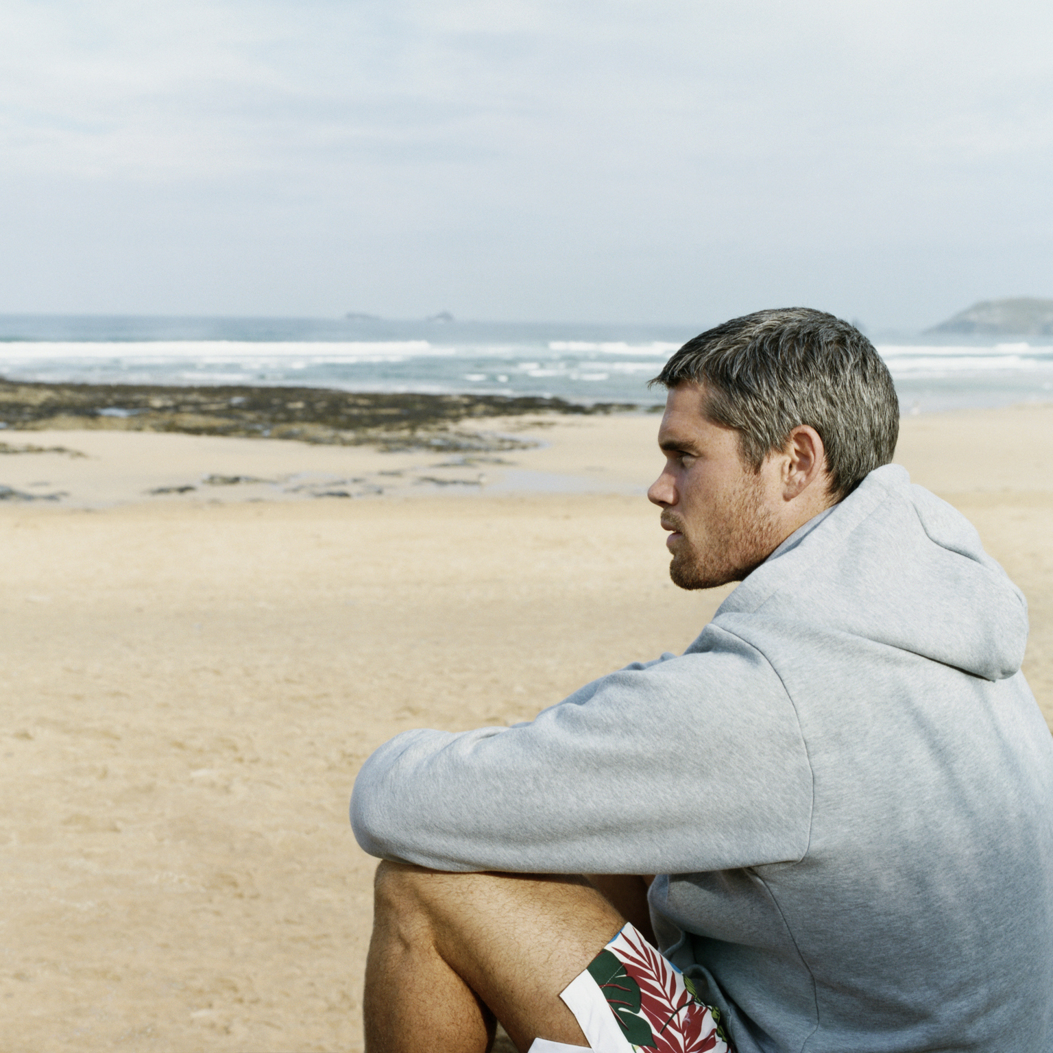 man sitting on a beach in a hoodie
