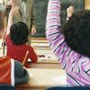 Children raising their hands in classroom during teacher's math lesson