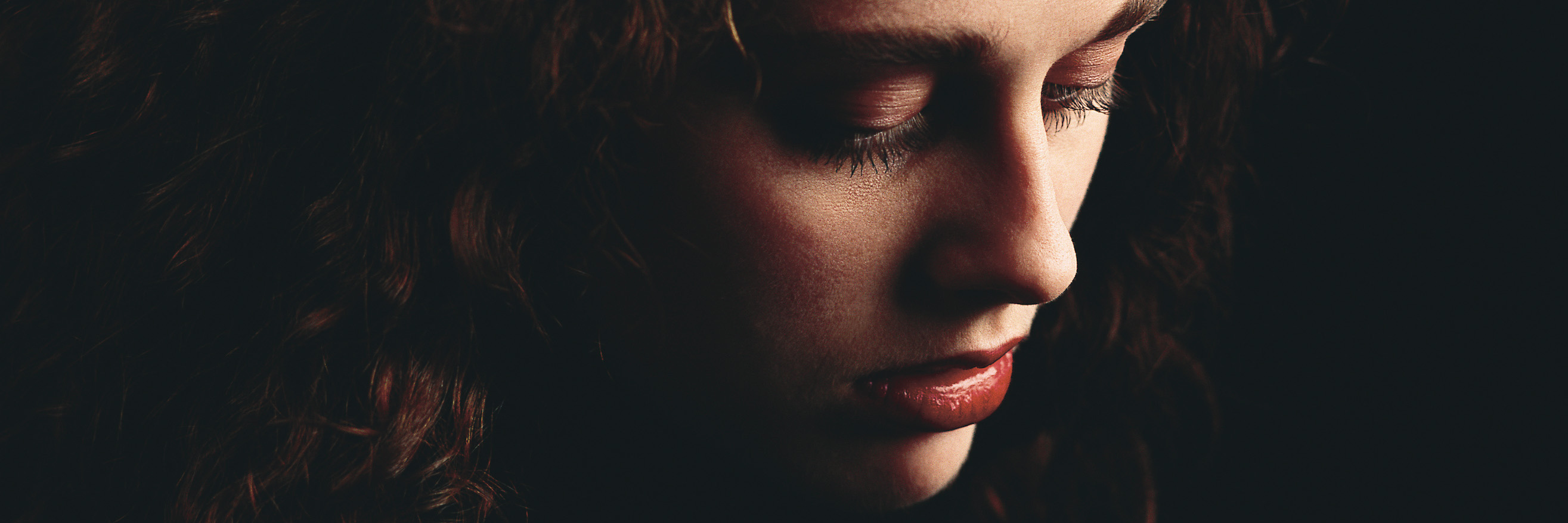 Why We Need to Talk About Binge Eating Disorder woman with brown hair in darkness looking sad