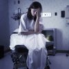 A worried patient sits in a hospital gown in a hospital room.