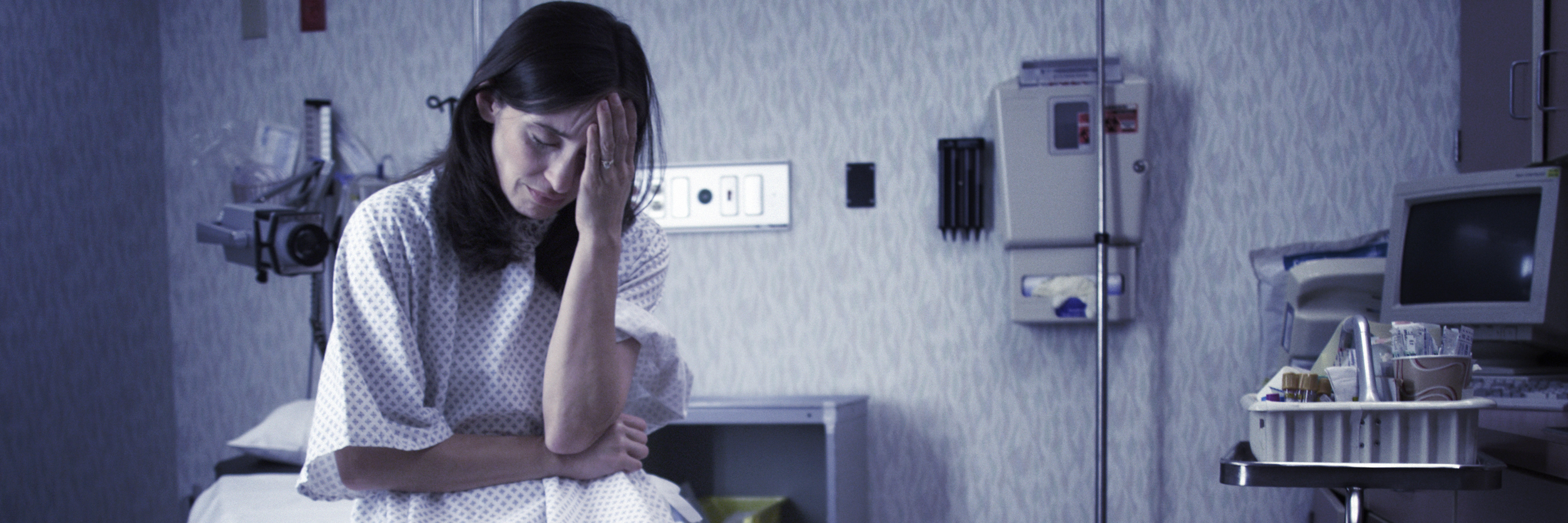 The Scary Trend I See in Our Health Care System A worried patient sits in a hospital gown in a hospital room.