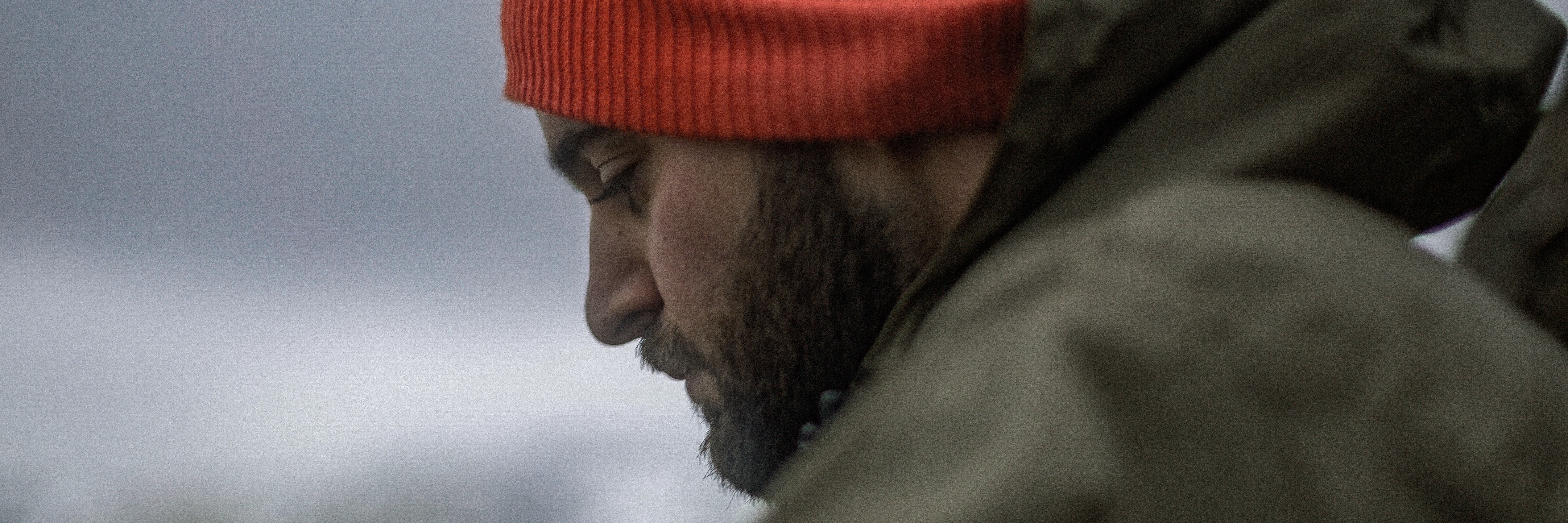 side view of man with beard and red hat looking down at ground depression