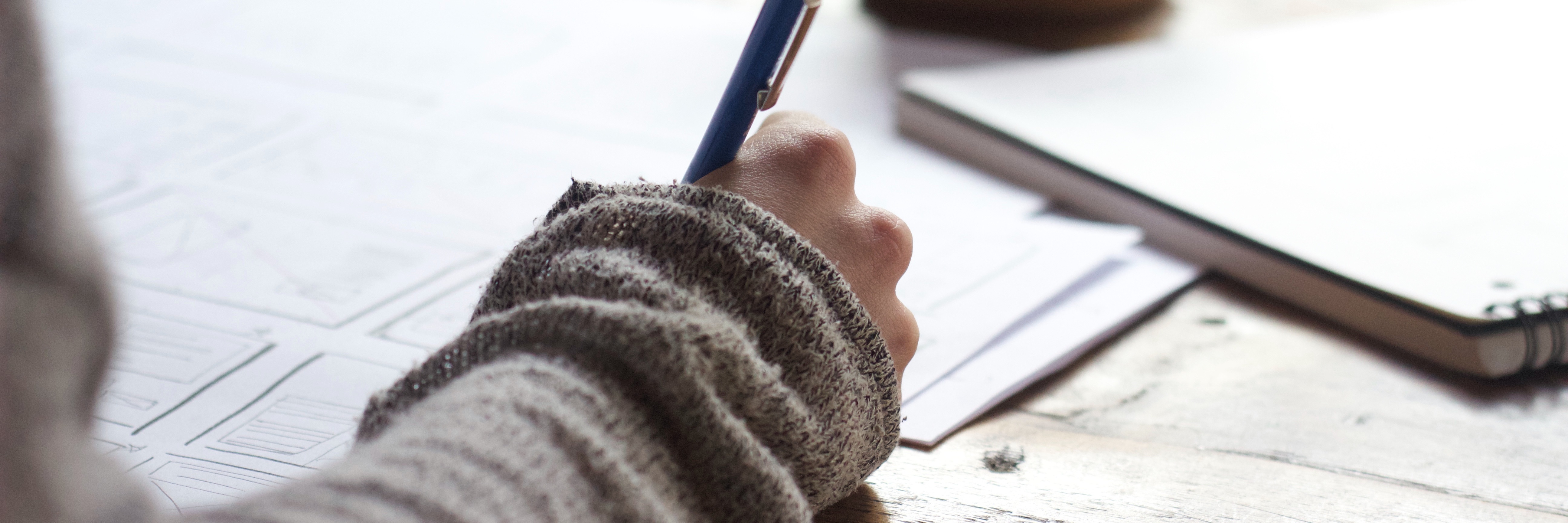 Does Mental Illness Help or Hinder the Writing Process? woman's hand holding pen over page with coffee mug in background, writer concept