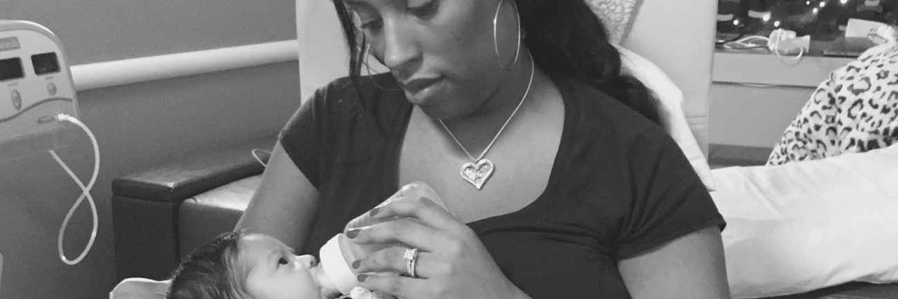 Mother holding her baby, giving her baby a bottle in a hospital room