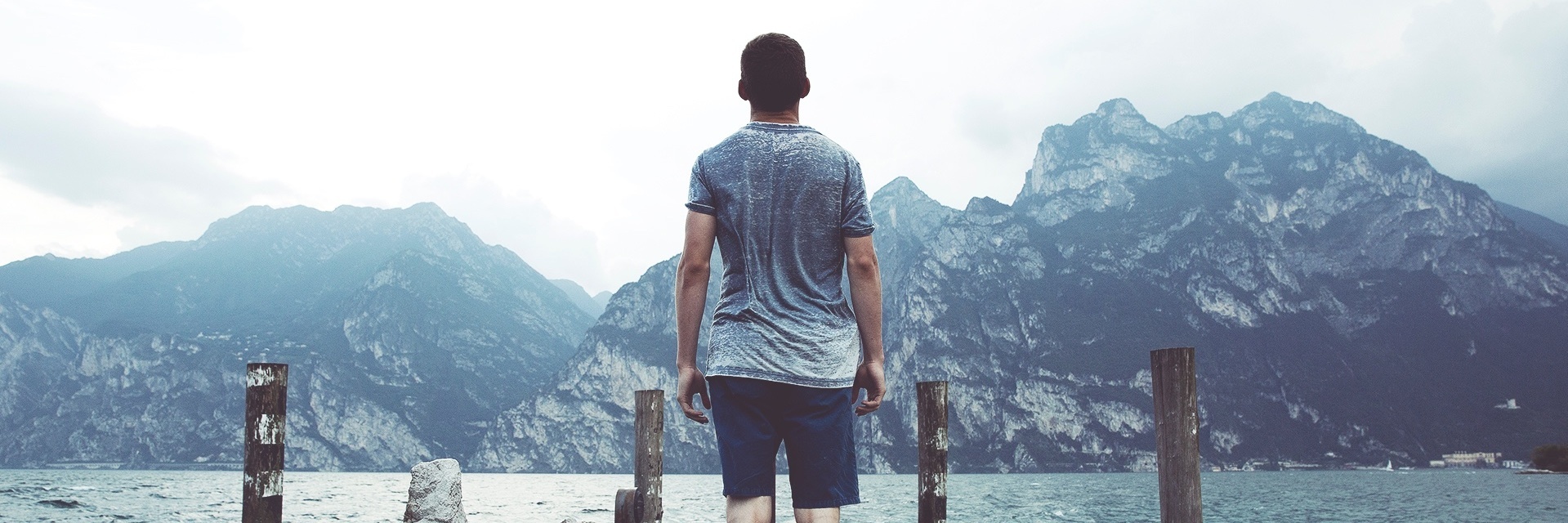 young man standing on pier looking out over water and distant mountains