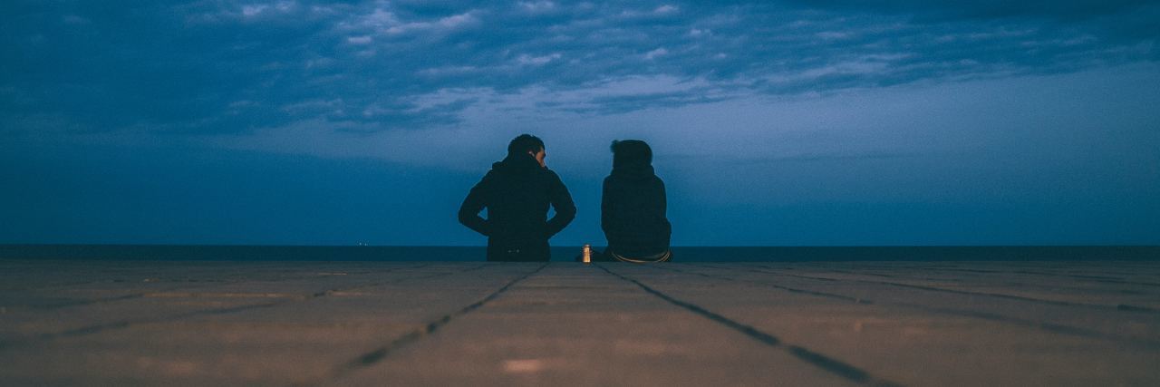 two people sitting at the end of a dock at night