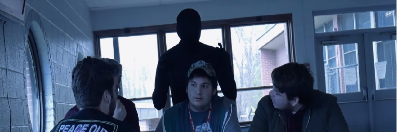 Zach Perry Creates 'PANIC' Short Film About What Anxiety Feels Like students at table with "anxiety"person in black morph suit