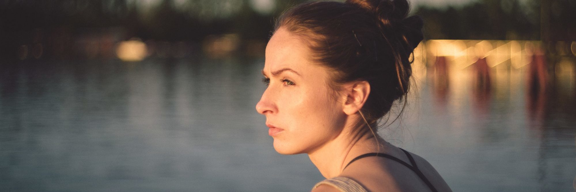 young woman in sunset by water staring out thoughtfully
