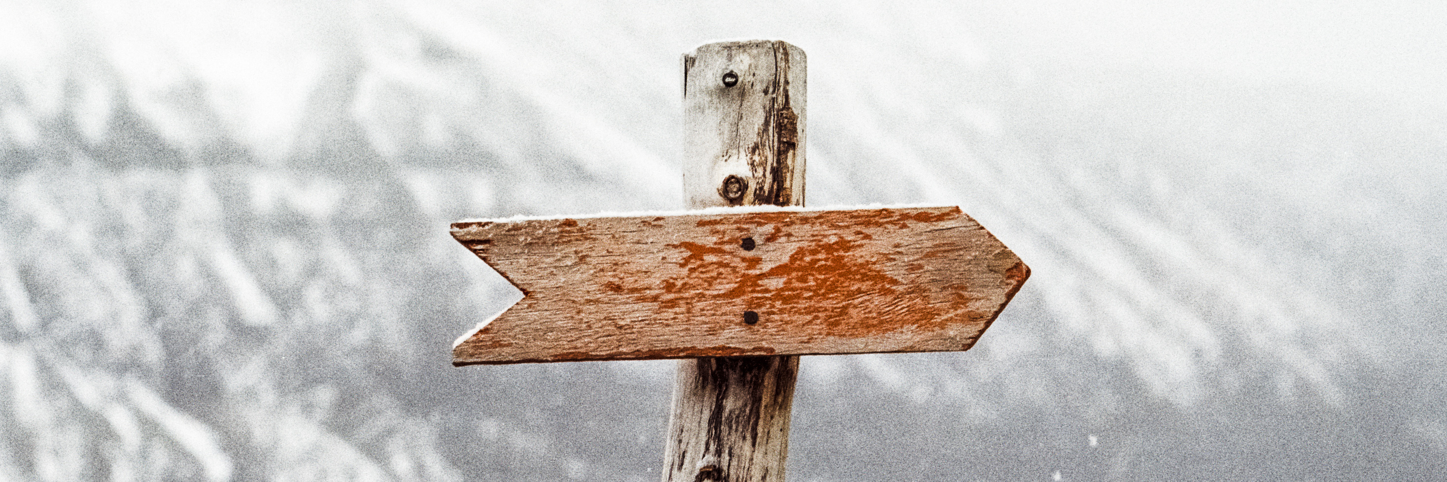 post with an arrow pointing right in front of a snowy mountain