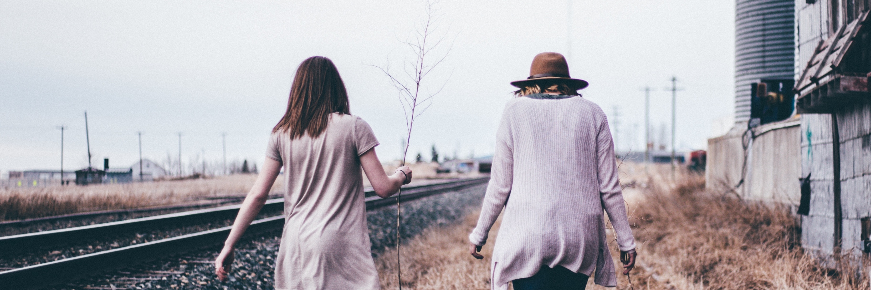 two women friends walking together alongside railway track past derelict house