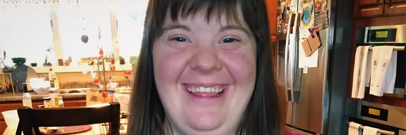 Woman with Down syndrome holdng floweres and smiling. She has brown hair and bangs.